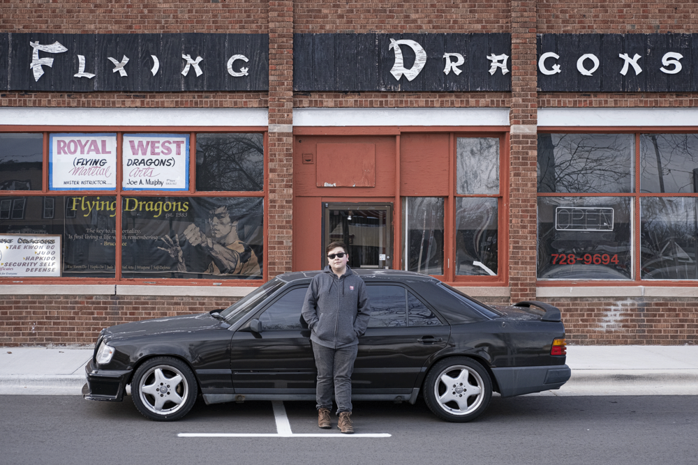 Angel Castenada leaning against the side of a Mercedes-Benz 300E outside of Delevan Flying Dragons martial arts location.