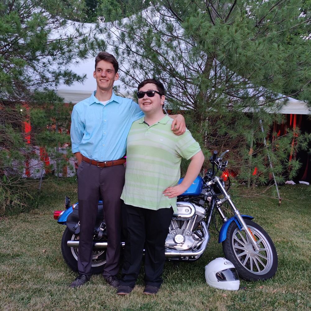 Angel Castenada and Alex Scerba standing in front of a Harley-Davidson Sportster 883 wearing casual dress atire.