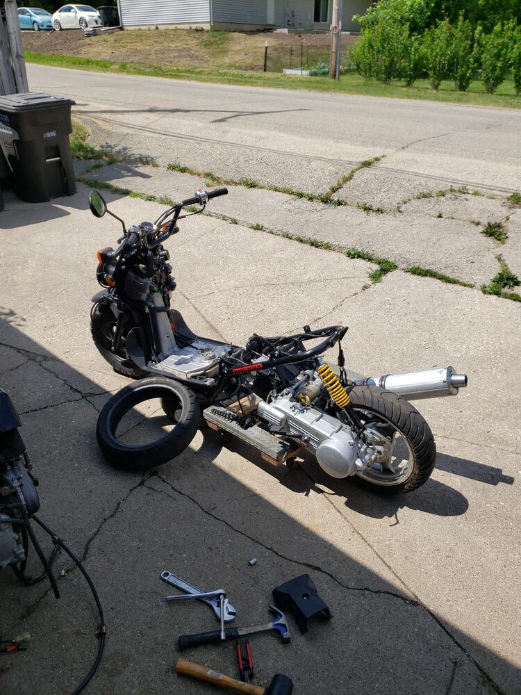 Left rear shot of a Honda Ruckus with a GY6 engine partially mounted to the frame resting on a dolly.