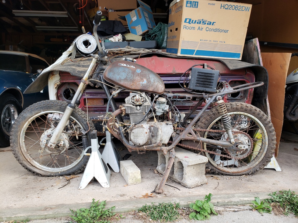 Very rusted stripped down Honda SL350 in front of a garage.