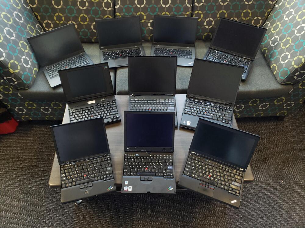 Group of ten Lenovo and IBM ThinkPads on table and couch.