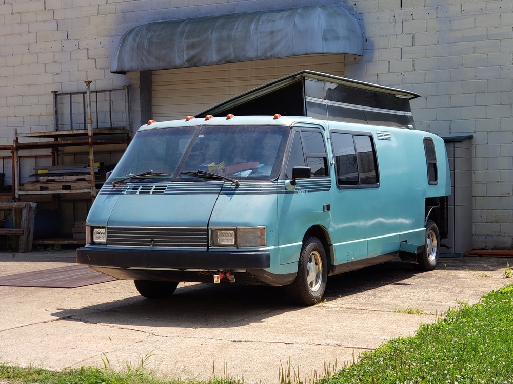 Picture of a light blue 80s Vixen 21TD motorhome in front of an industrial garage.