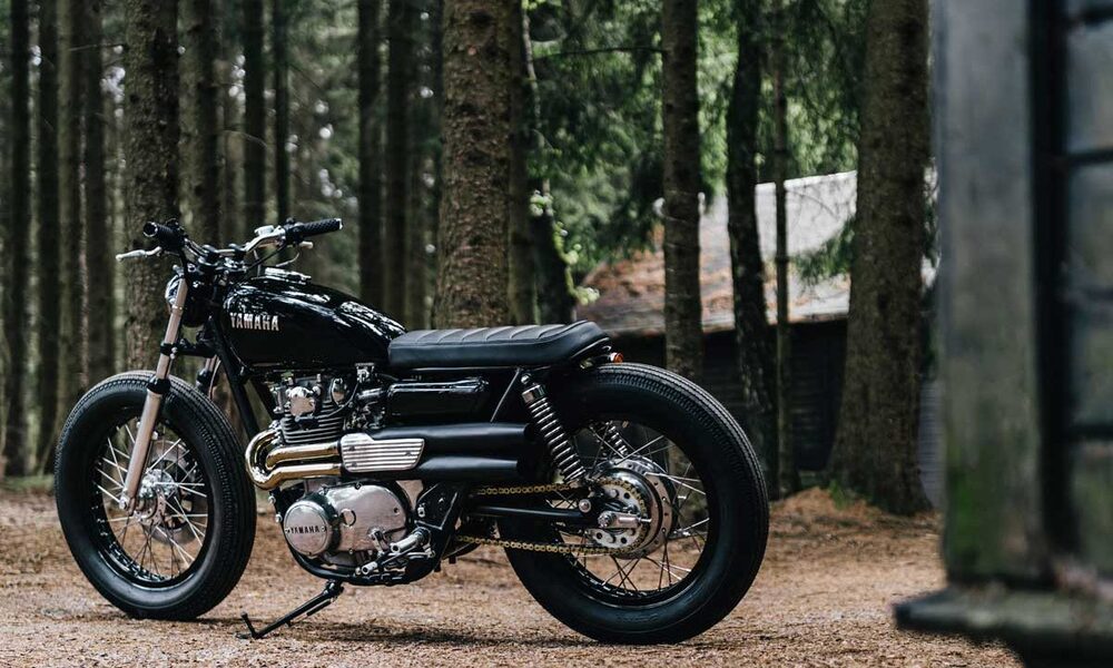 Left side shot of a 1974 XS650 painted black with silver suspension and engine sitting in a wooded area.